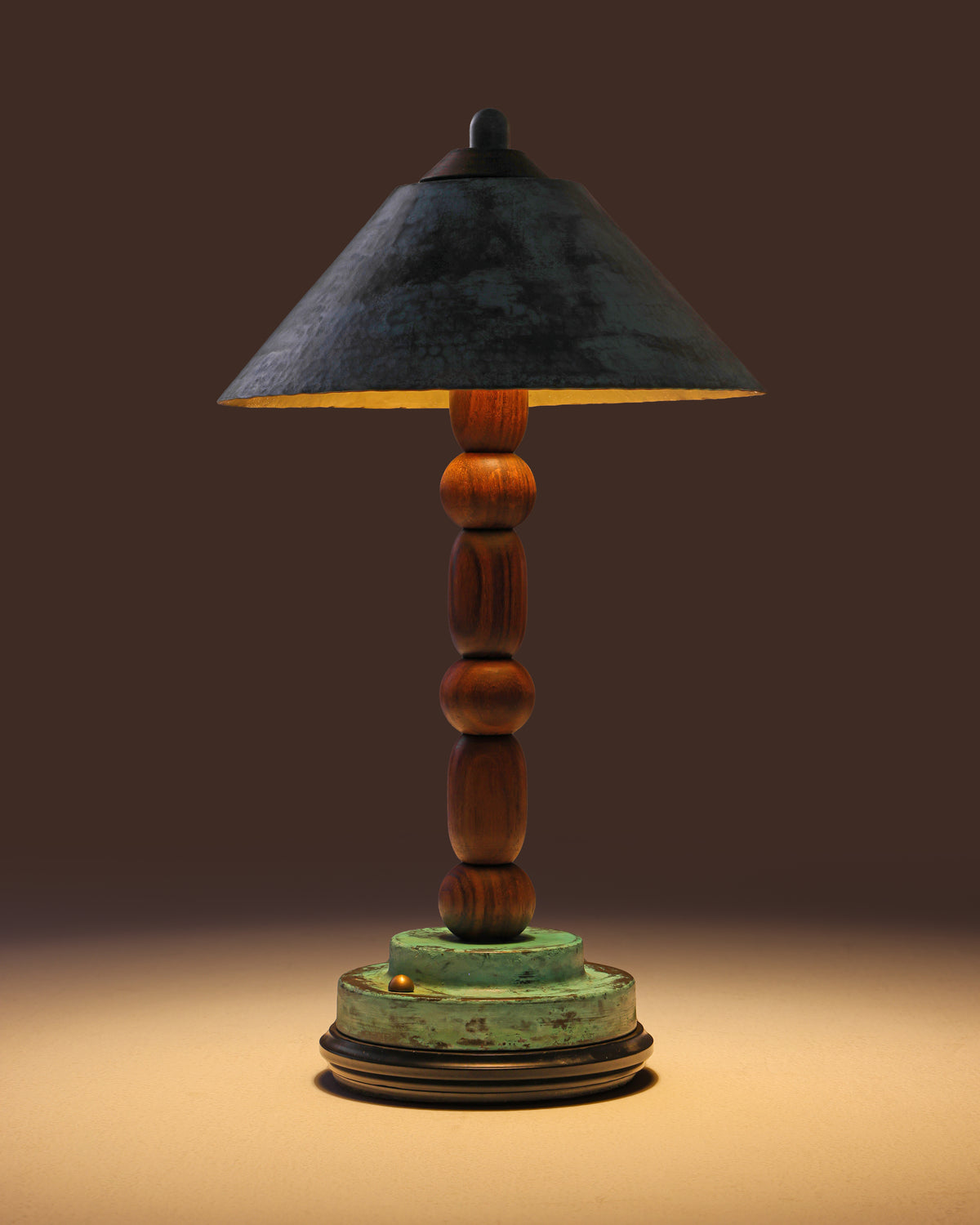 Totem II lamp lit, warm light falling from the brass shade onto the base